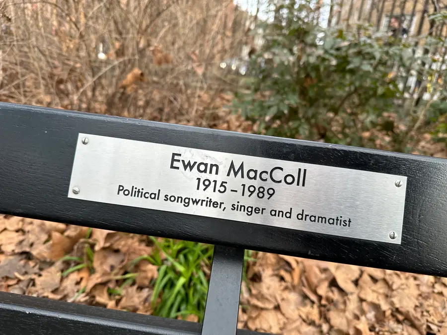 Metal plaque on a black park bench reading Ewan MacColl 1915 to 1989, political songwriter, singer and dramatist