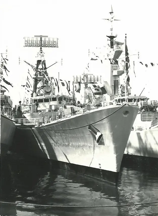 The grey frigate HMS Mohawk dressed overall with signal flags, alongside at Devonport, in black and white